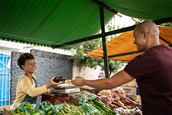 Young man handing an eggplant to the seller at a street market